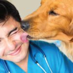 A man with his tongue out licking the nose of a dog.