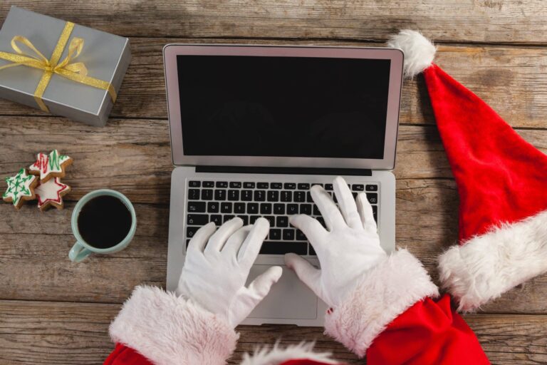 A person in santa claus outfit using laptop on wooden table.