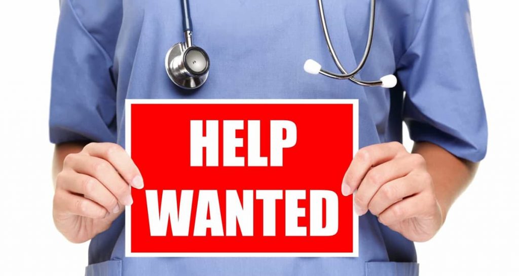 A nurse holding a sign that says "Help Wanted".